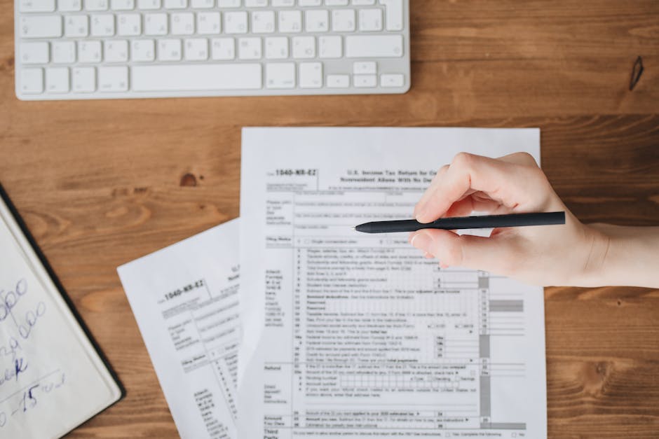 Close-up of a hand holding a pen over US tax forms on a wooden table.